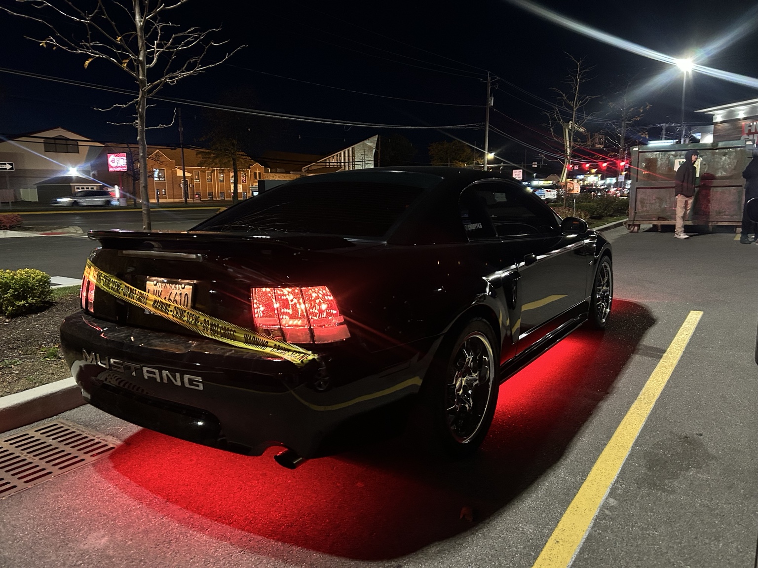 Rear three-quarter view of a black Mustang with red underglow